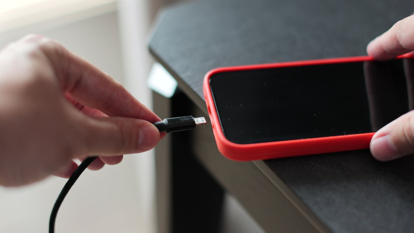 A person struggling to plug a charging cable into an iPhone that won't charge, illustrating common charging issues.